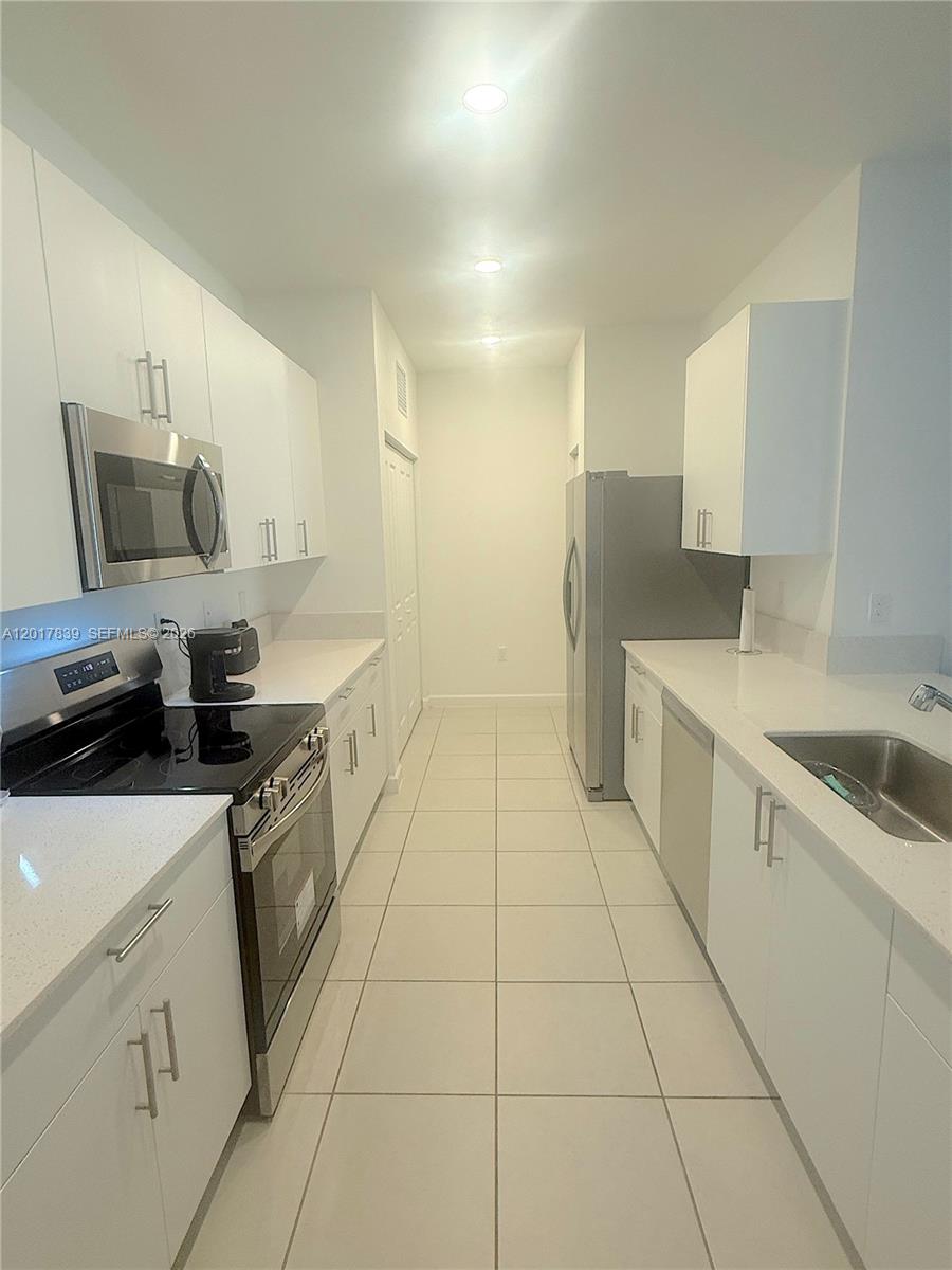 A galley-style kitchen features white cabinets, stainless steel appliances, and light-colored floor tiles — 4941 Oakmont Dr # 5838, Dania Beach FL 33312, DANIA BEACH, FL