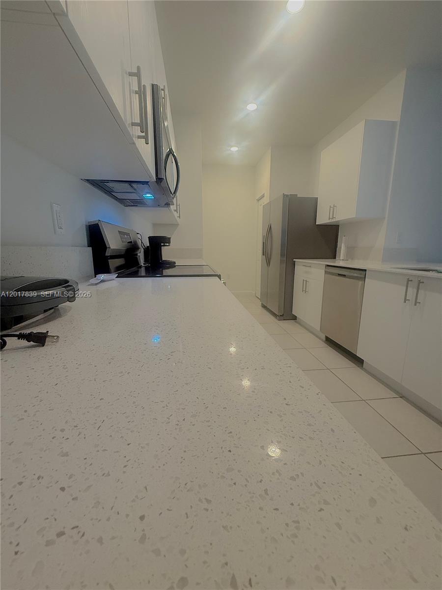 A galley kitchen features white cabinets, quartz countertops, and stainless steel appliances — 4941 Oakmont Dr # 5838, Dania Beach FL 33312, DANIA BEACH, FL