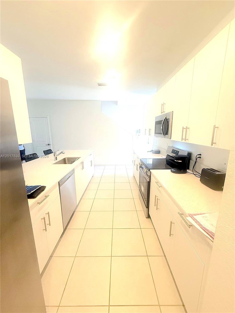 A galley-style kitchen features white cabinets, light countertops, and tiled flooring — 4941 Oakmont Dr # 5838, Dania Beach FL 33312, DANIA BEACH, FL