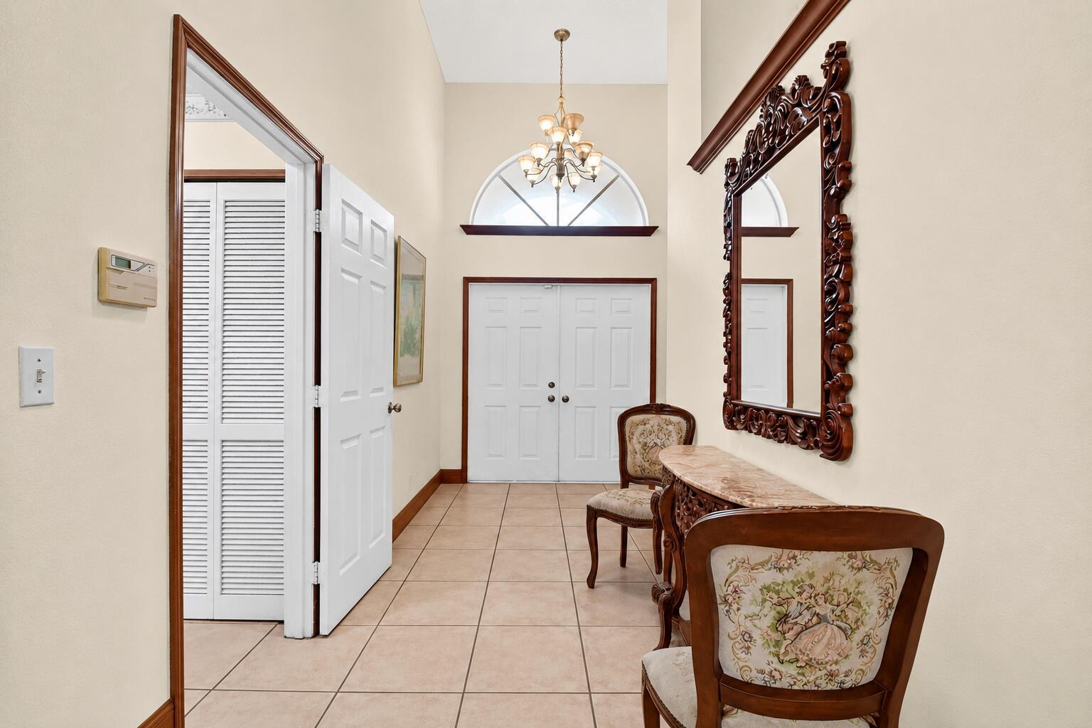 An entryway features tile flooring, a chandelier, a console table with a mirror, and double doors — 1059 Fairfax Circle W, Boynton Beach FL 33436, BOYNTON BEACH, FL
