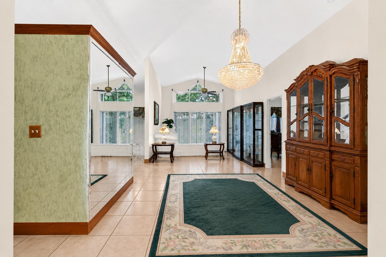 A spacious room features tile flooring, a large crystal chandelier, and a wooden china cabinet — 1059 Fairfax Circle W, Boynton Beach FL 33436, BOYNTON BEACH, FL