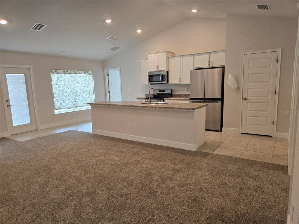 A kitchen with white cabinets, stainless steel appliances, and a central island overlooks a carpeted room — 825 W HALLAM DRIVE, CITRUS SPRINGS, FL