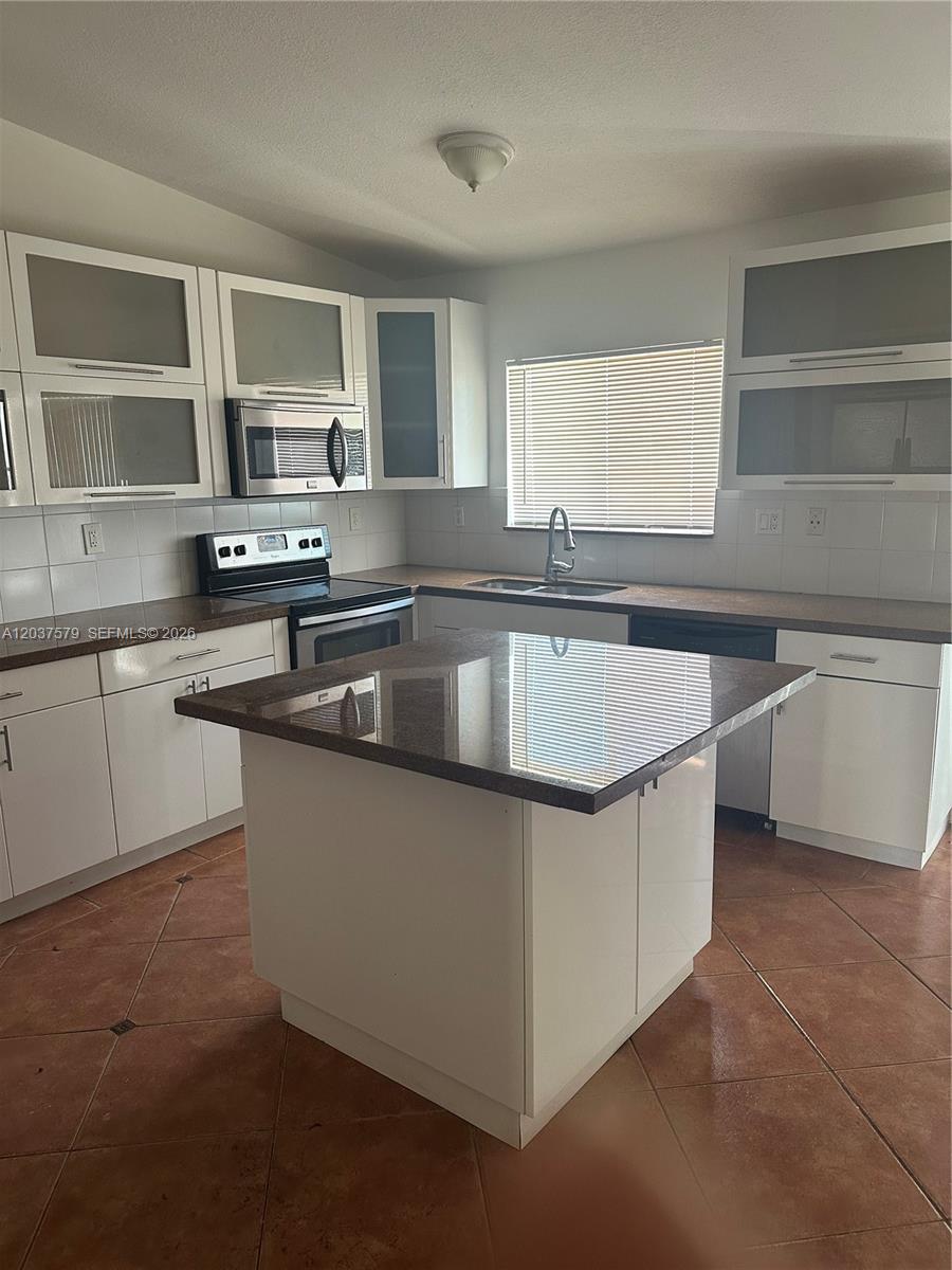 A kitchen features white cabinets, a dark granite island, and tiled flooring — 12855 SW 207th Ter, Miami FL 33177, MIAMI, FL