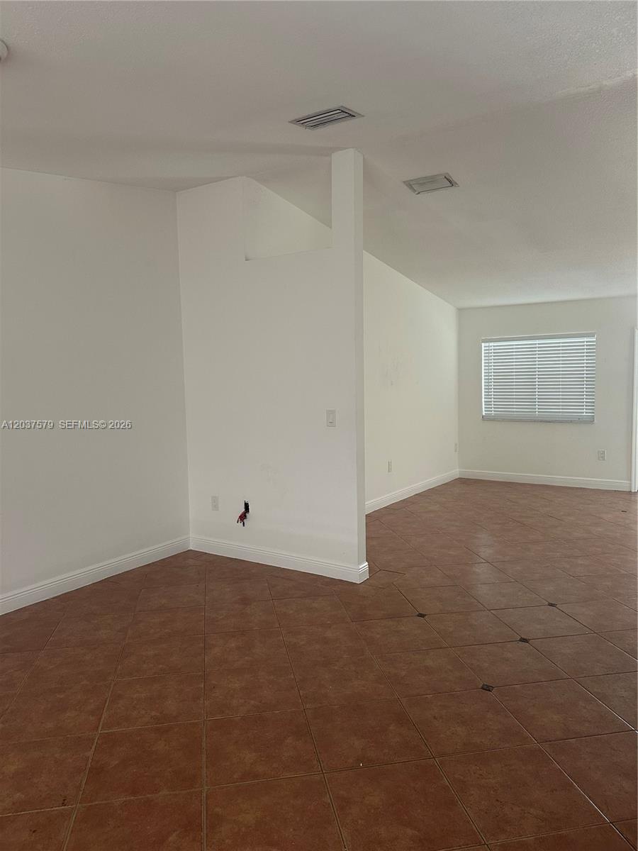 An empty room features white walls, tan tile flooring, and a partial partition wall — 12855 SW 207th Ter, Miami FL 33177, MIAMI, FL
