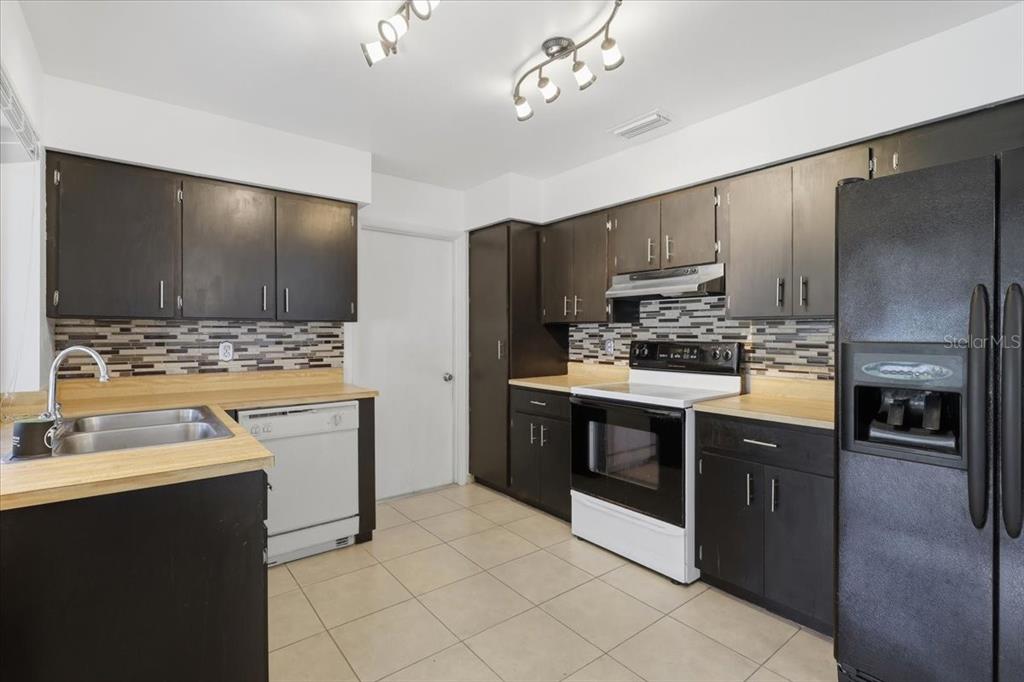 A kitchen with dark cabinets, light countertops, a tiled backsplash, and black appliances — 10 FENWICK LANE, PALM COAST, FL