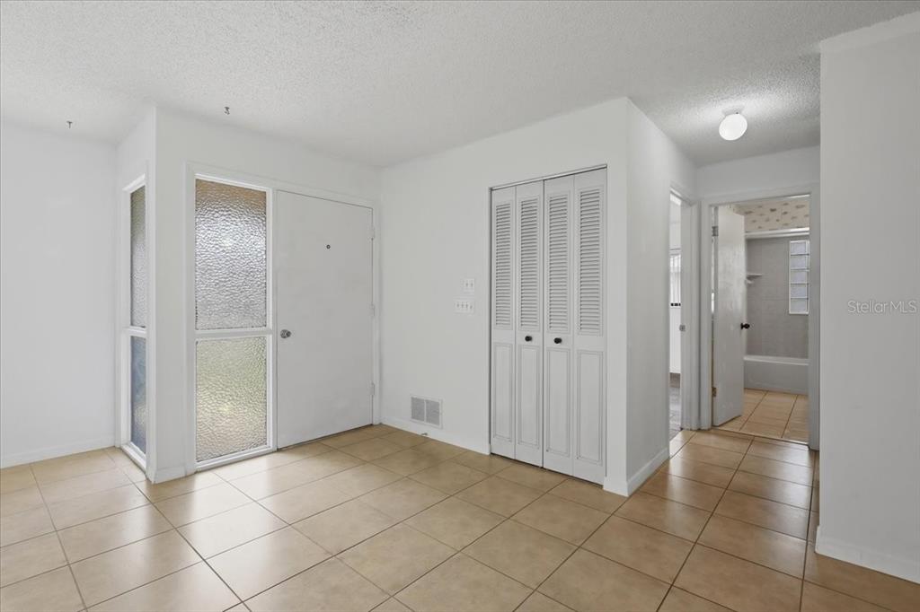 An entryway with beige tile flooring, a white front door, and a louvered closet door — 10 FENWICK LANE, PALM COAST, FL