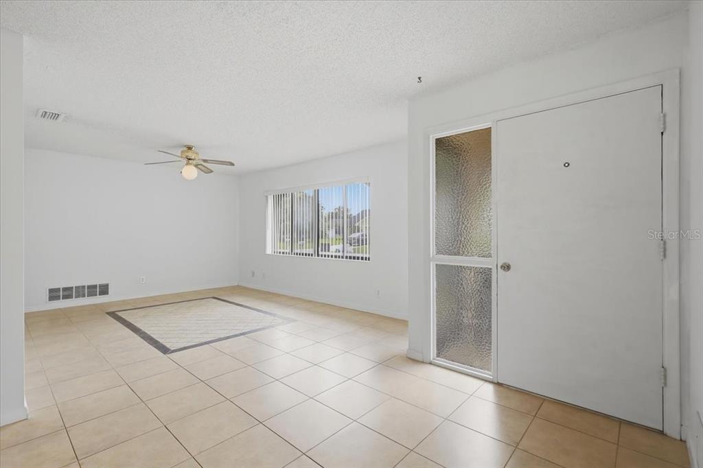 A bright living room features white walls, tile flooring, a ceiling fan, and a front door — 10 FENWICK LANE, PALM COAST, FL