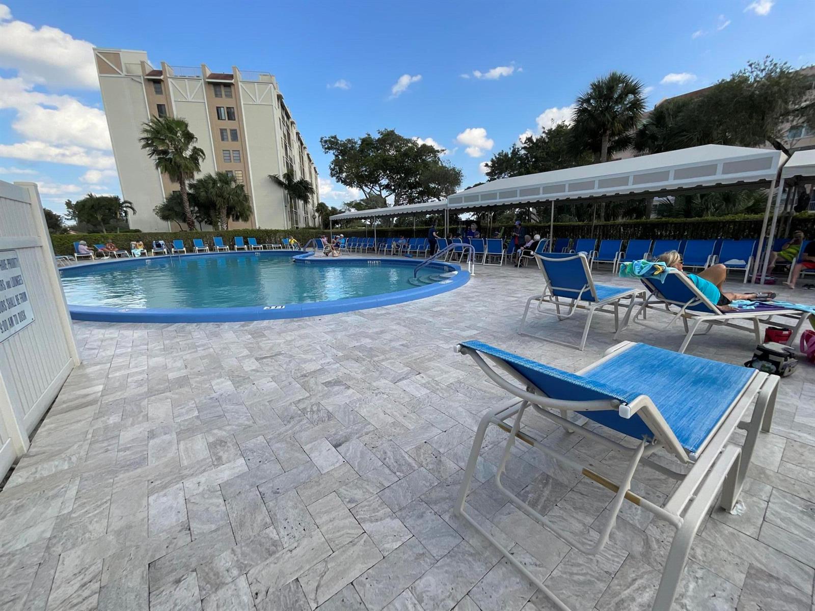 A swimming pool with lounge chairs on a stone patio next to a tall building — 14475 Strathmore Lane # 501, Delray Beach FL 33446, DELRAY BEACH, FL