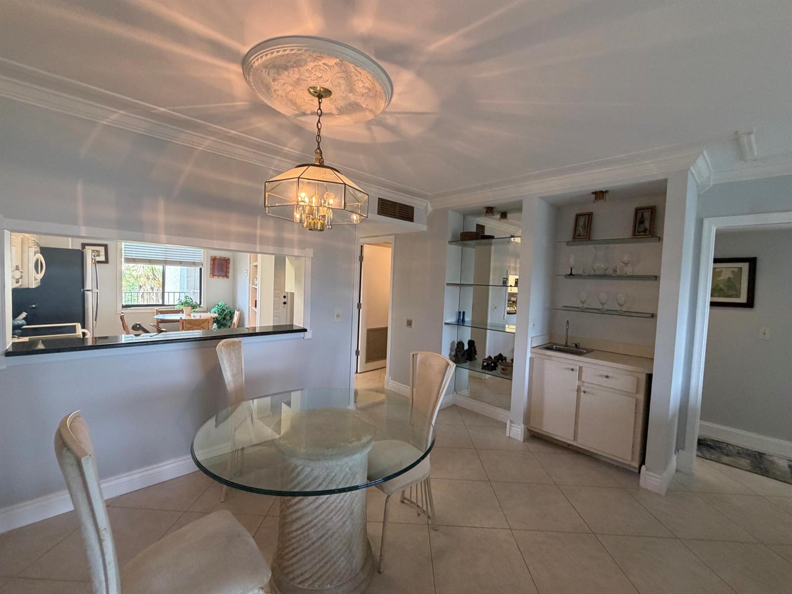 A dining area features a glass table, a chandelier, and a built-in wet bar — 14475 Strathmore Lane # 501, Delray Beach FL 33446, DELRAY BEACH, FL