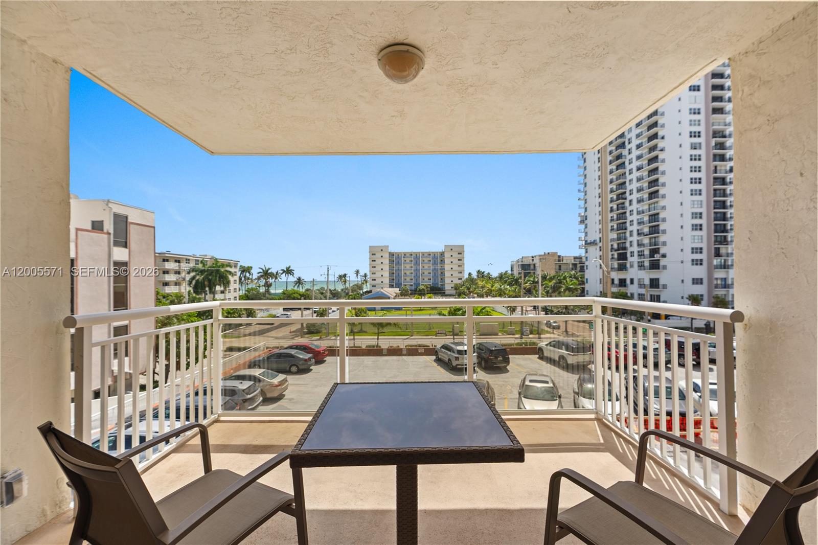 A balcony with a table and chairs overlooks a parking lot and distant ocean view — 1600 S Ocean Dr # 4G, Hollywood FL 33019, HOLLYWOOD, FL