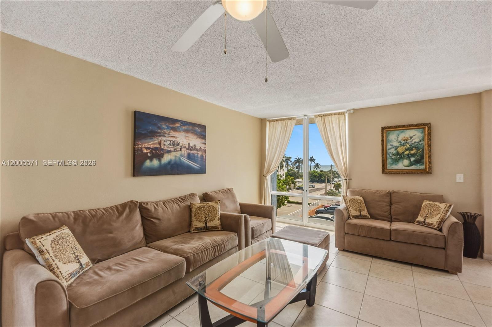 A living room features beige sofas, a glass coffee table, and a view of palm trees — 1600 S Ocean Dr # 4G, Hollywood FL 33019, HOLLYWOOD, FL