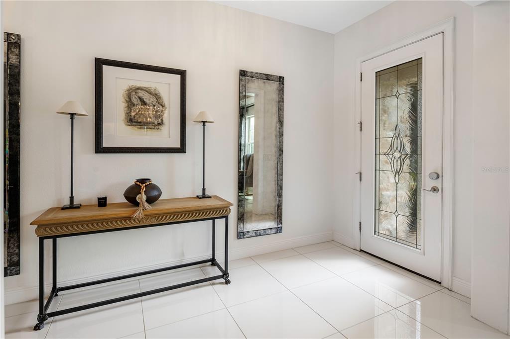 A bright entryway features white tile floors, a console table, wall mirrors, and a glass-paneled door — 8419 KARWICK STREET, ORLANDO, FL