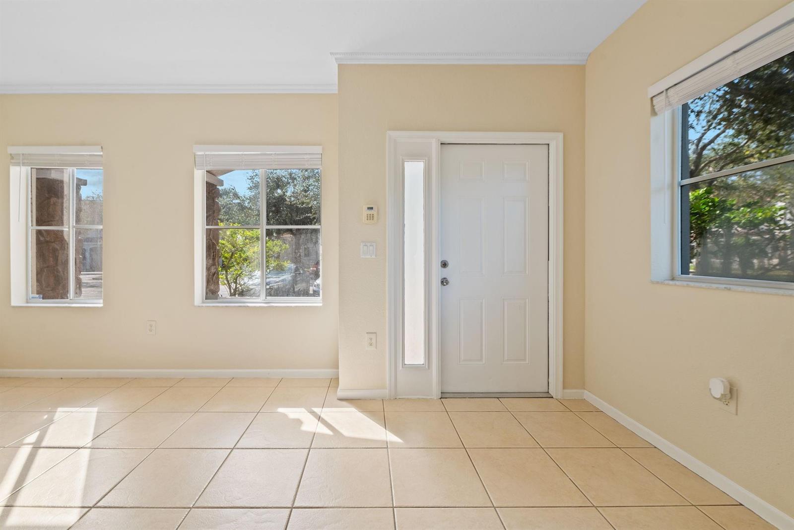 An empty room with beige tile flooring, light-colored walls, and a white front door — 8299 SW 27th Street # 101, Miramar FL 33025, MIRAMAR, FL
