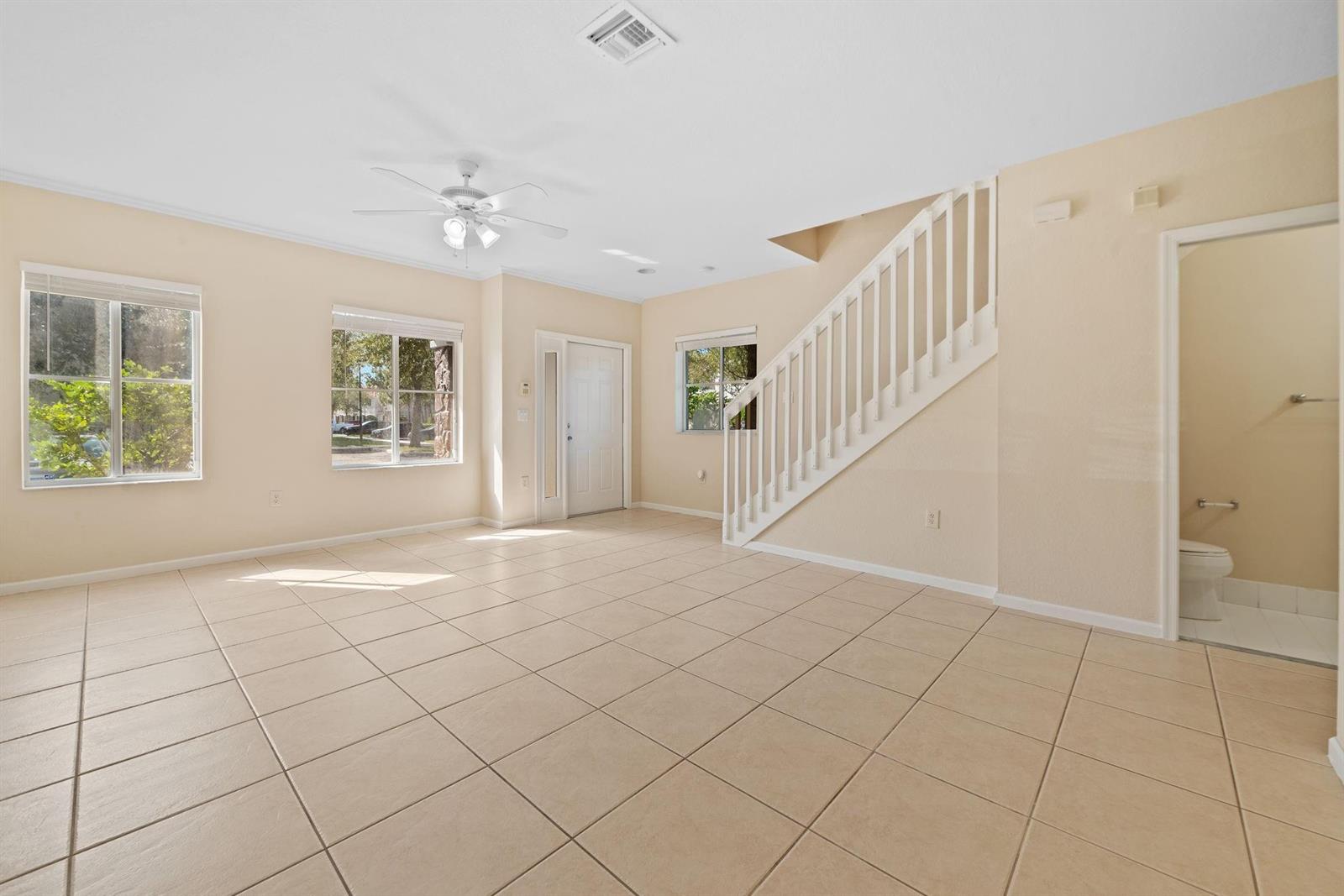 An empty living room features beige tile flooring, a white staircase, and a ceiling fan — 8299 SW 27th Street # 101, Miramar FL 33025, MIRAMAR, FL