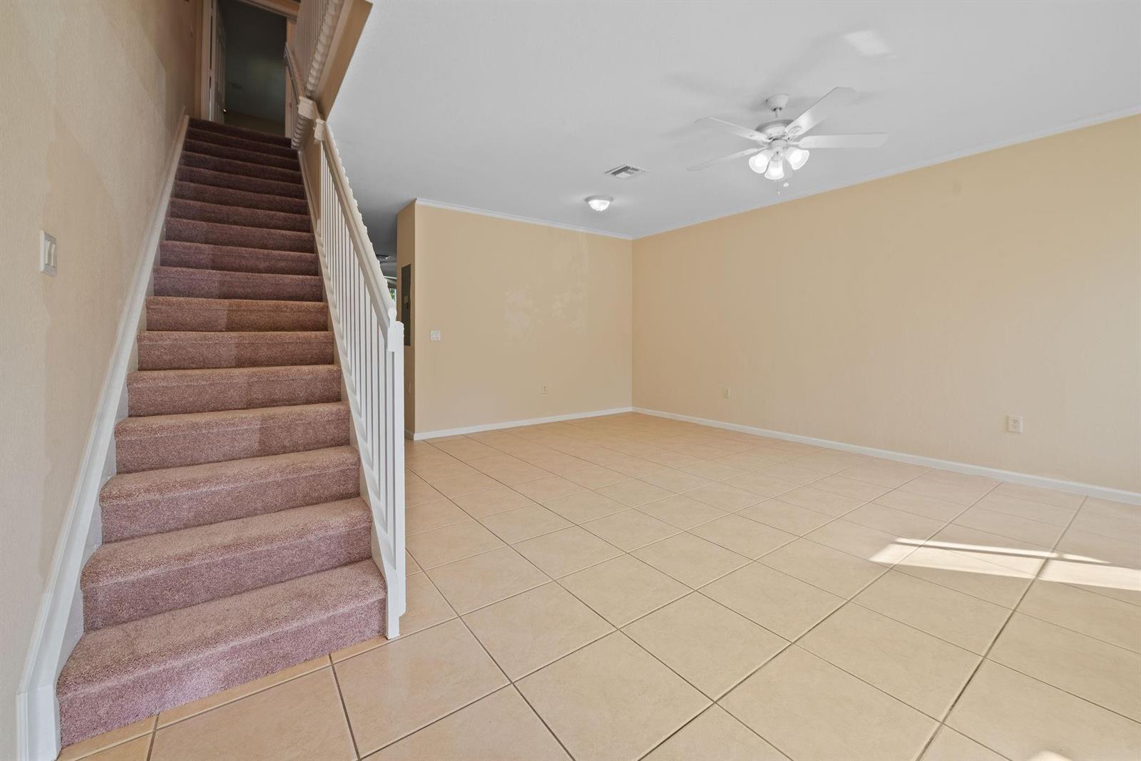 A carpeted staircase leads upstairs next to an empty living room with tiled floors — 8299 SW 27th Street # 101, Miramar FL 33025, MIRAMAR, FL