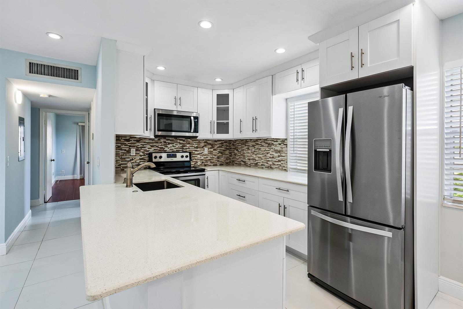 A modern kitchen features white cabinetry, stainless steel appliances, a quartz island, and mosaic backsplash — 507 Capri K, Delray Beach FL 33484, DELRAY BEACH, FL
