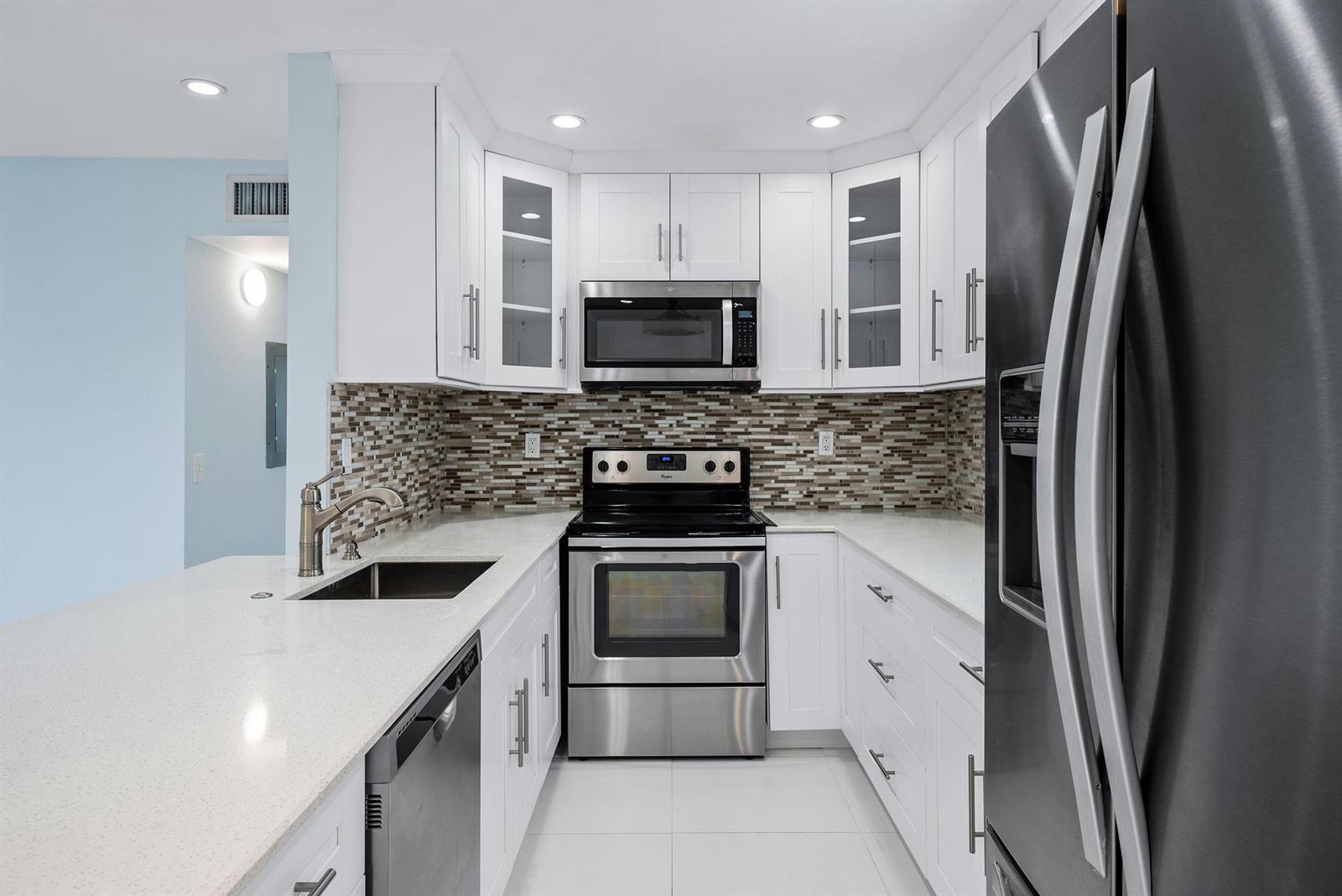 A modern kitchen features white cabinets, stainless steel appliances, and a mosaic tile backsplash — 507 Capri K, Delray Beach FL 33484, DELRAY BEACH, FL