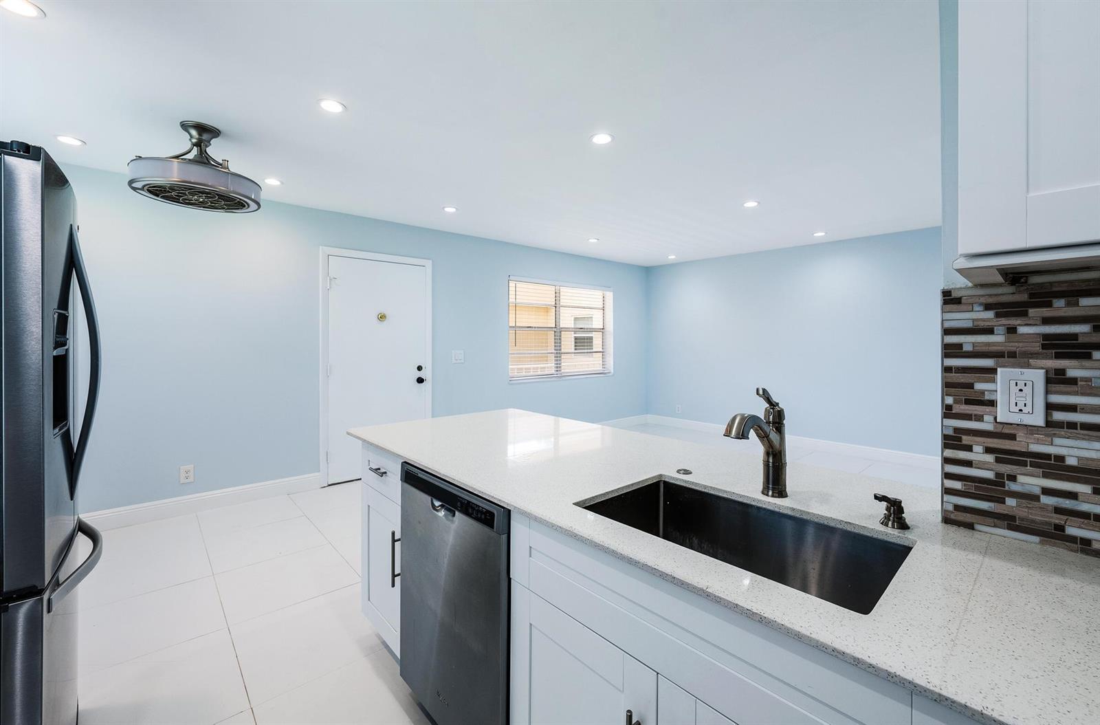 A kitchen with white cabinets, a quartz island, a stainless steel sink, and light blue walls — 507 Capri K, Delray Beach FL 33484, DELRAY BEACH, FL