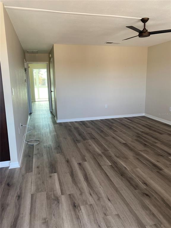An empty room with wood-look flooring, a ceiling fan, and a hallway leading to a porch — 11100 86TH AVENUE UNIT 307, SEMINOLE, FL