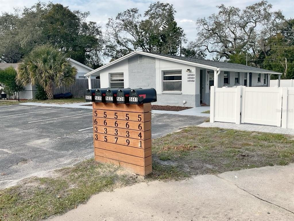 A wooden post holds five mailboxes in front of a single-story gray residential building — 5633 GOLDEN NUGGET DRIVE, HOLIDAY, FL