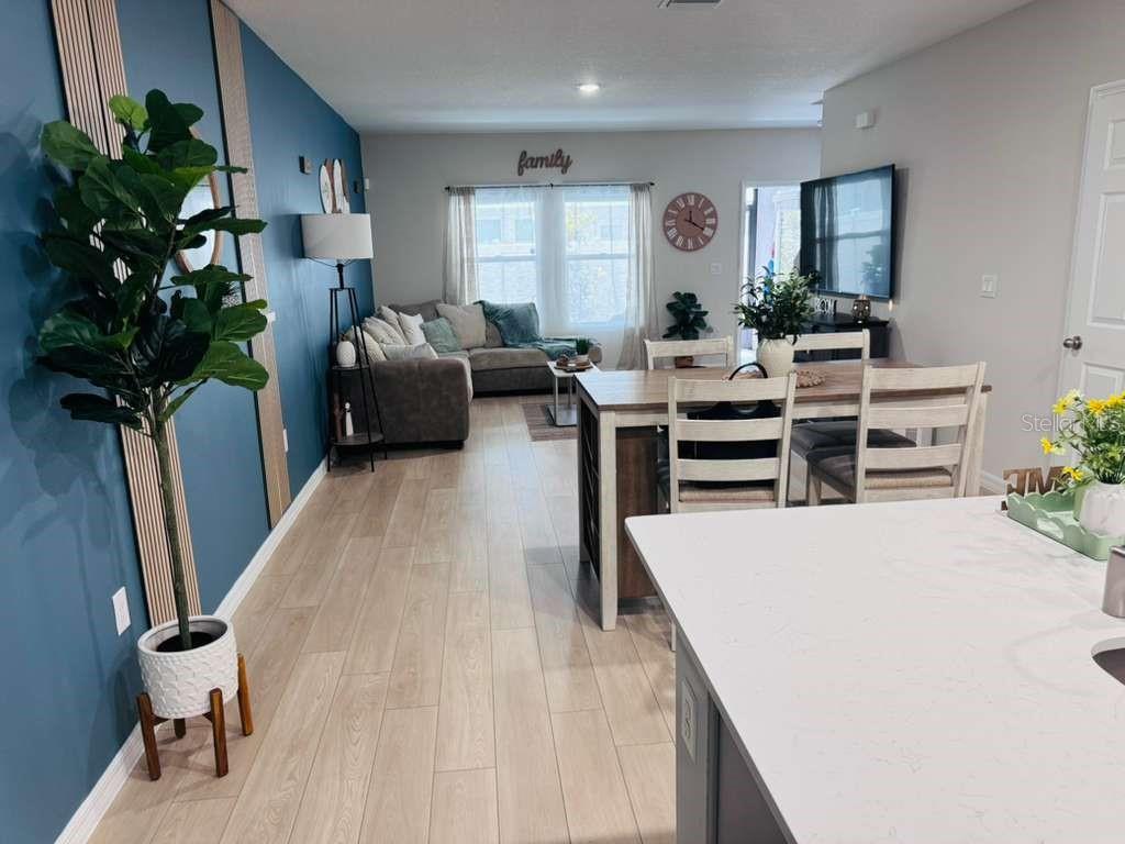 An open-concept living and dining area features wood-look flooring, a blue accent wall, and furniture — 3840 KING HILL DRIVE, HAINES CITY, FL