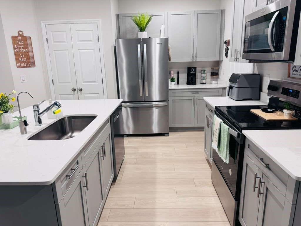 A modern kitchen features gray cabinets, stainless steel appliances, and a white quartz island countertop — 3840 KING HILL DRIVE, HAINES CITY, FL