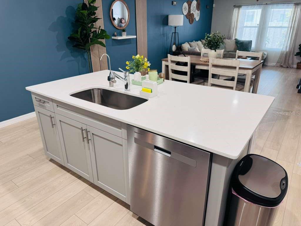 A kitchen island with a stainless steel sink, dishwasher, and white countertop faces a dining area — 3840 KING HILL DRIVE, HAINES CITY, FL