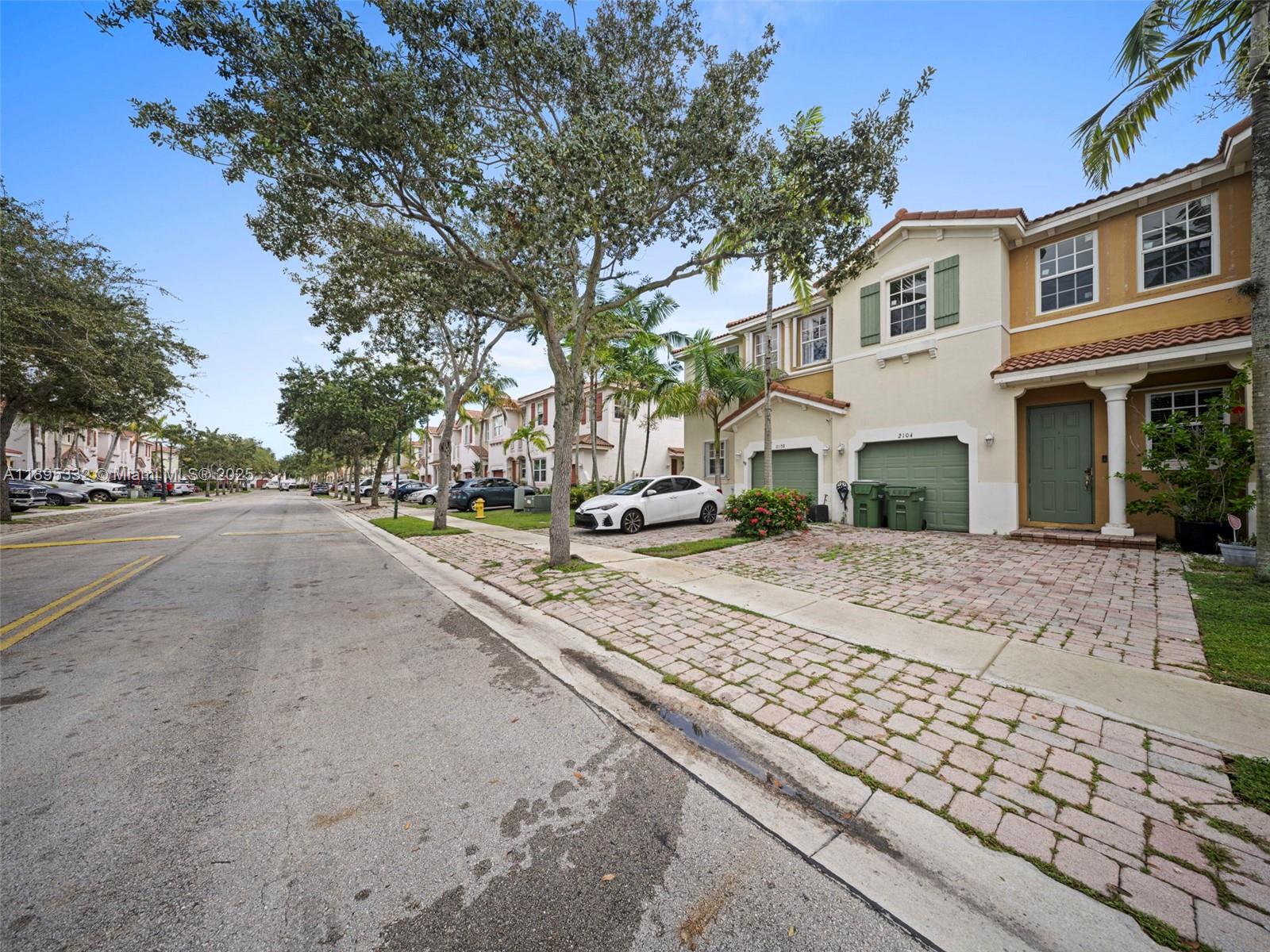 A street view of a residential neighborhood featuring multi-story townhomes with paved driveways and trees — 2104 NE 3rd Ct, Homestead FL 33033, HOMESTEAD, FL
