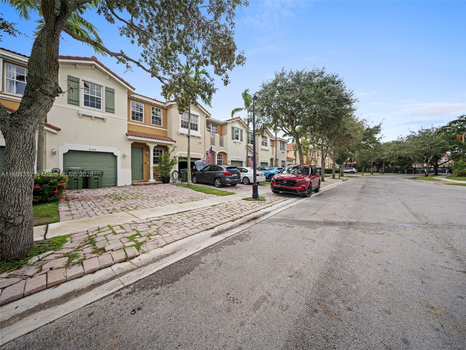 A row of two-story townhomes with paved driveways and parked cars lines a suburban street — 2104 NE 3rd Ct, Homestead FL 33033, HOMESTEAD, FL