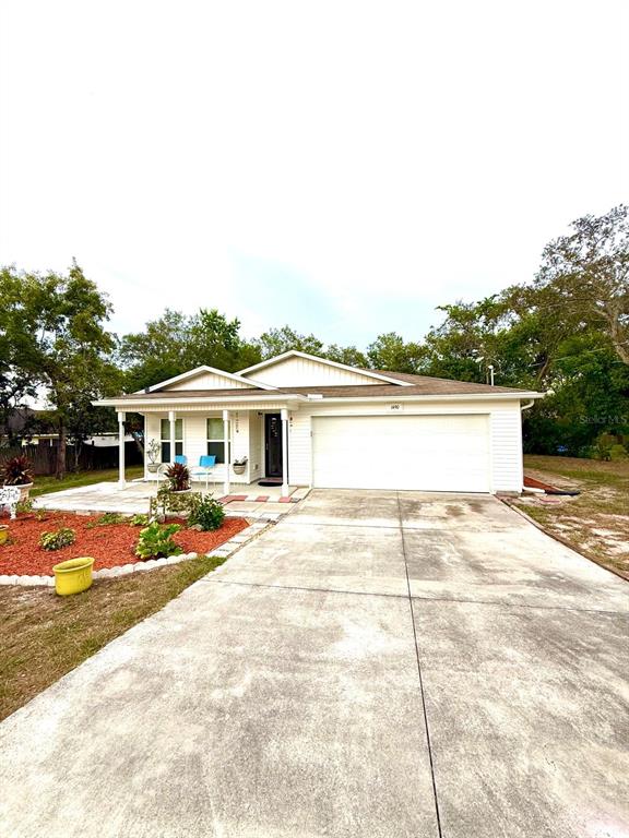 A single-story house with a white exterior sits behind a lawn with two garden beds — 1490 PIPER ROAD, SPRING HILL, FL