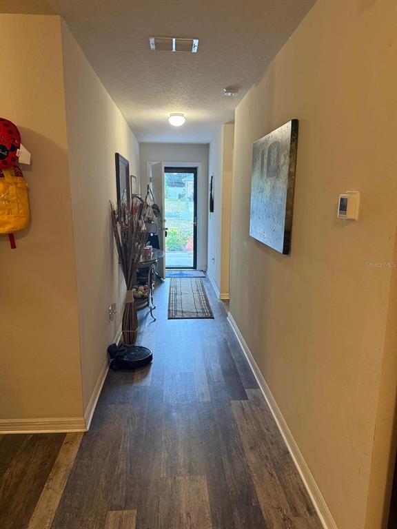A hallway with wood-look flooring leads past a kitchen area with a stainless steel refrigerator — 1490 PIPER ROAD, SPRING HILL, FL
