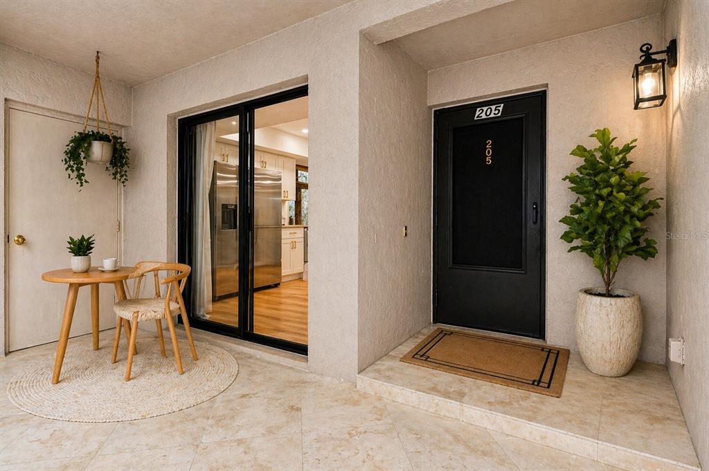 A covered patio features a small dining set, a black front door, and potted plants — 1055 KENSINGTON PARK DRIVE UNIT 205, ALTAMONTE SPRINGS, FL