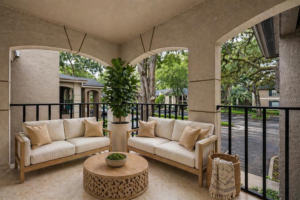 A covered balcony features two beige sofas, a round wooden coffee table, and a potted plant — 1055 KENSINGTON PARK DRIVE UNIT 205, ALTAMONTE SPRINGS, FL