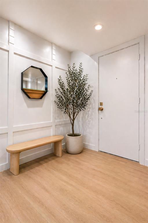 An entryway features a light wood bench, a potted olive tree, and a wall mirror — 1055 KENSINGTON PARK DRIVE UNIT 205, ALTAMONTE SPRINGS, FL