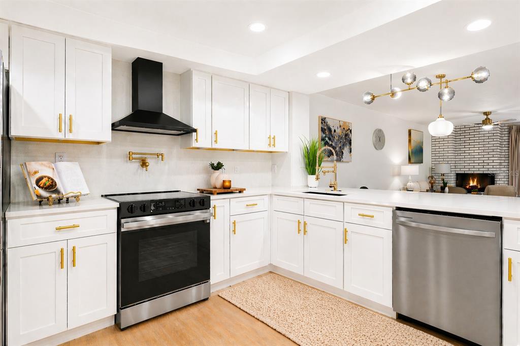 A modern kitchen features white cabinets, gold hardware, stainless steel appliances, and a black range hood — 1055 KENSINGTON PARK DRIVE UNIT 205, ALTAMONTE SPRINGS, FL