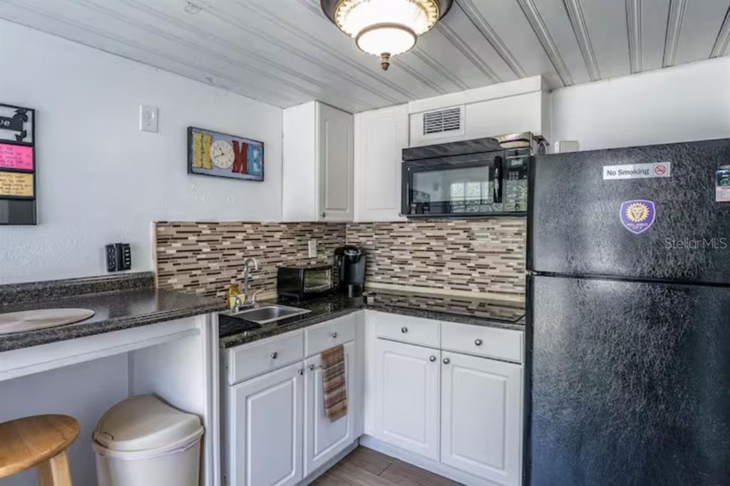A small kitchen features white cabinets, a black refrigerator, a microwave, and a tiled backsplash — 2014 NEWMAN ST UNIT 2, ORLANDO, FL