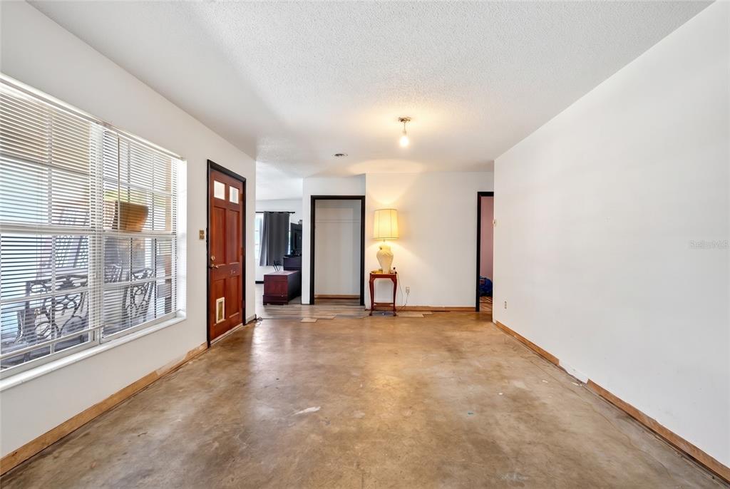 An empty room with concrete floors, white walls, a wooden door, and a table lamp — 6174 SE 125TH PLACE, BELLEVIEW, FL