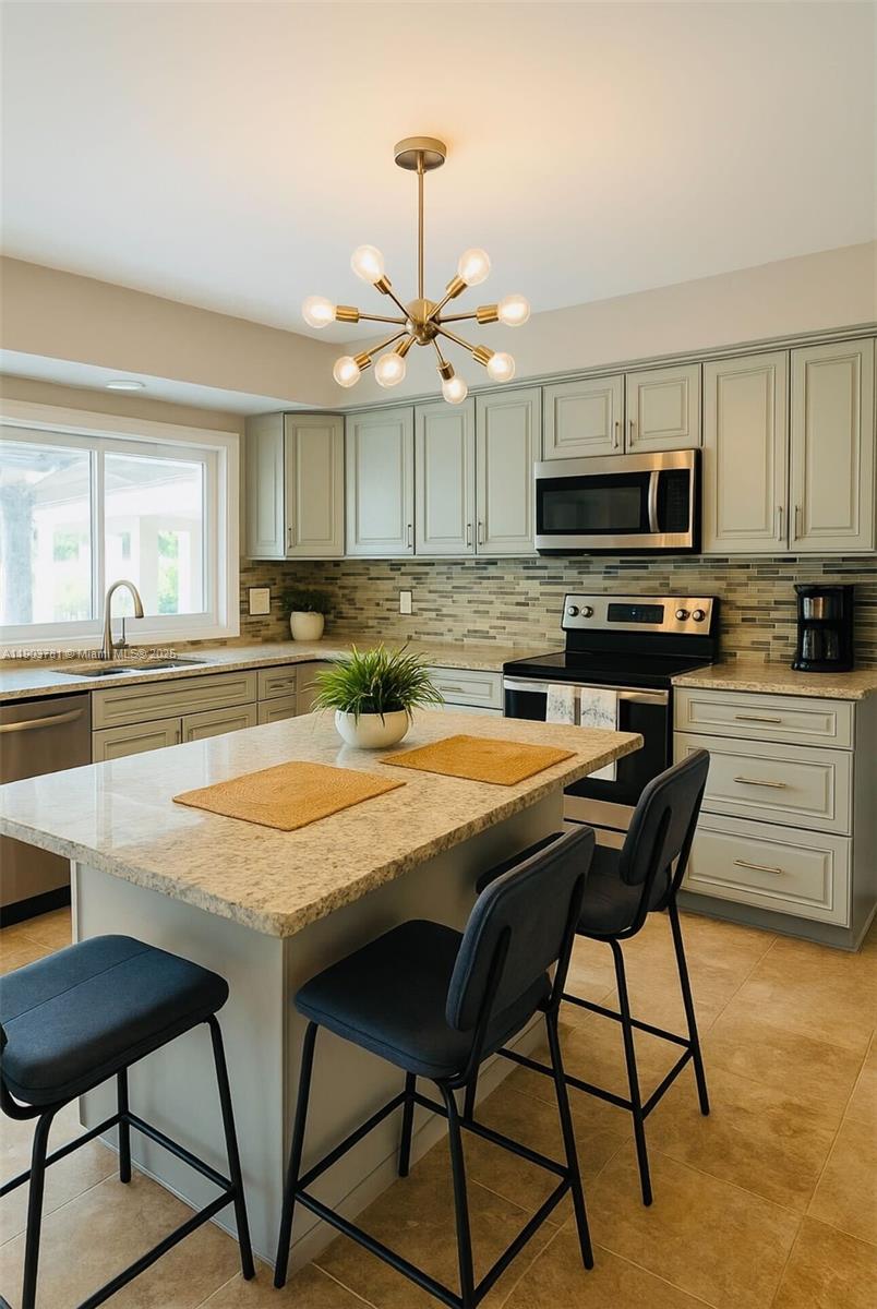 A kitchen features light-colored cabinetry, granite countertops, a central island with stools, and a chandelier — 6391 SW 34th St, Miramar FL 33023, MIRAMAR, FL