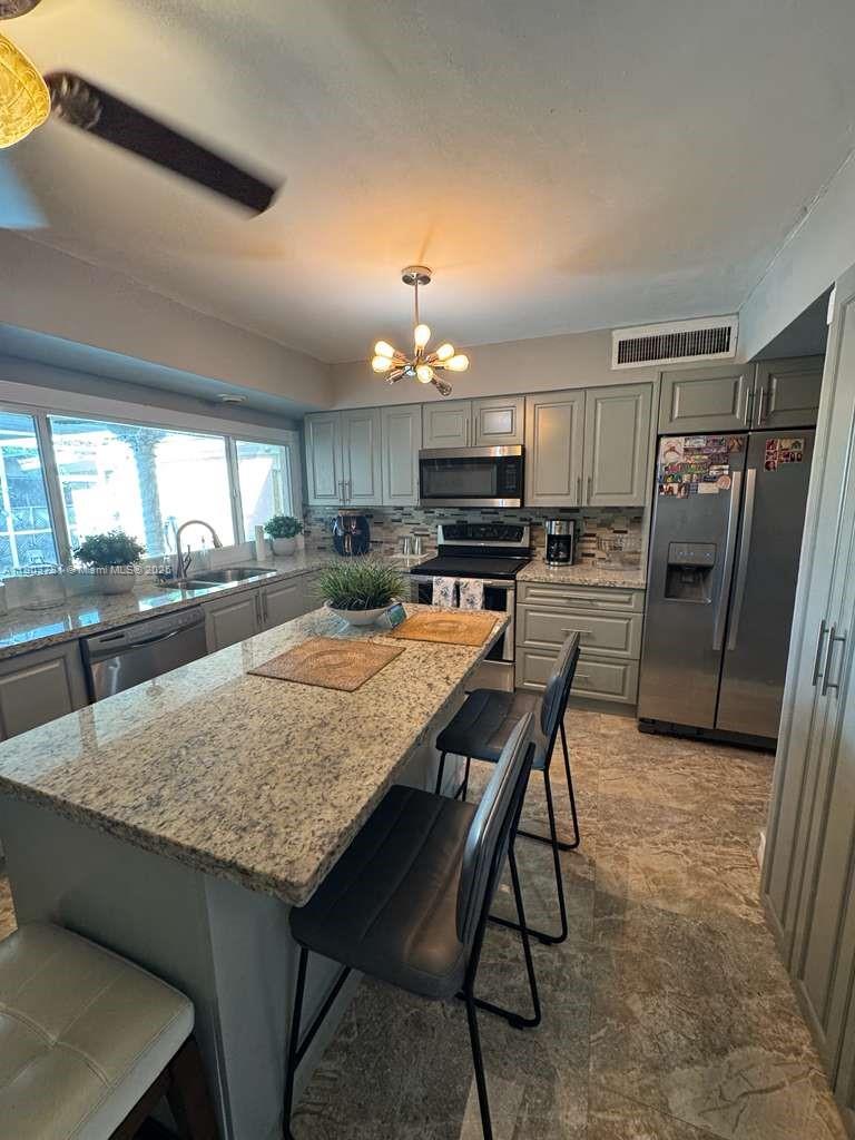 A kitchen features gray cabinets, granite countertops, a central island with seating, and stainless appliances — 6391 SW 34th St, Miramar FL 33023, MIRAMAR, FL