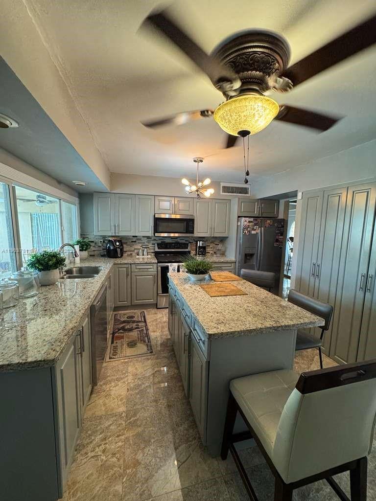 A kitchen features gray cabinetry, granite countertops, a central island, and a ceiling fan — 6391 SW 34th St, Miramar FL 33023, MIRAMAR, FL