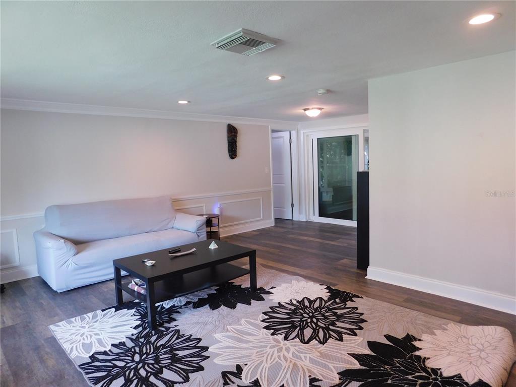A living room features light gray walls, wood-look flooring, a floral area rug, and a sofa — 8020 HUNTERS WHIP ROW, HUDSON, FL