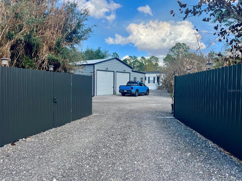 A gravel driveway leads to a metal garage and a house behind a fenced gate — 345 N HACIENDA STREET, CLEWISTON, FL