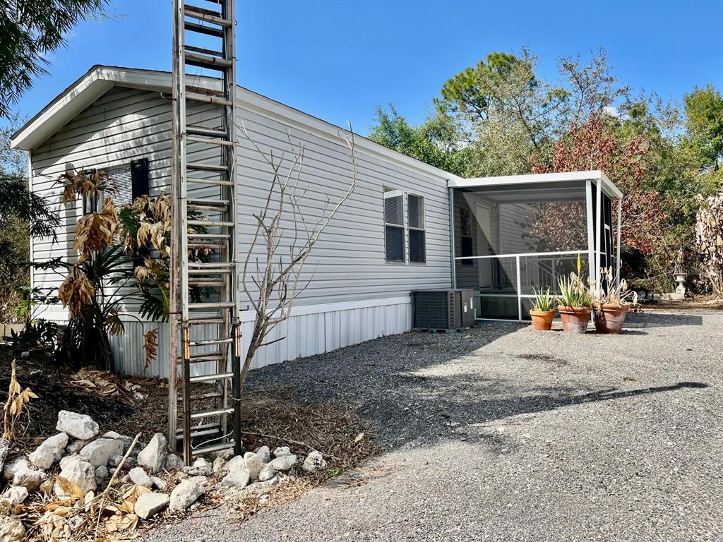 A single-story manufactured home with light gray siding, a screened porch, and a metal ladder — 345 N HACIENDA STREET, CLEWISTON, FL