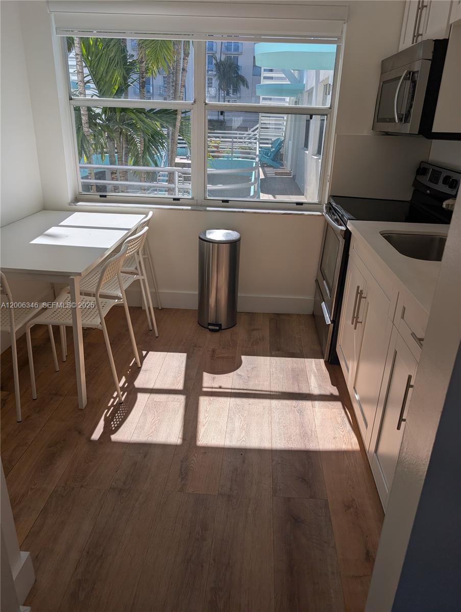 A small kitchen features white cabinets, stainless steel appliances, and a dining table by a window — 326 Wilson St # 201, Hollywood FL 33019, HOLLYWOOD, FL