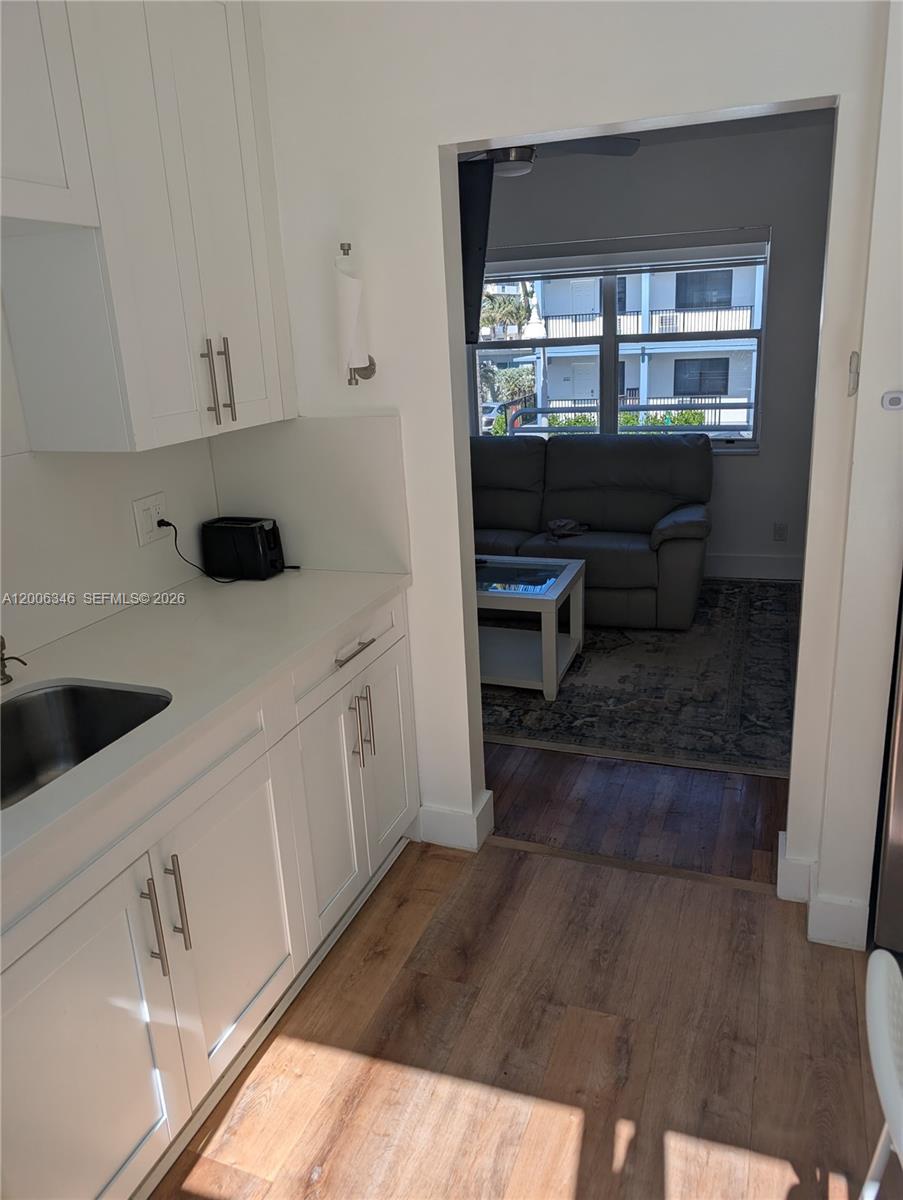 A white kitchen with a sink and cabinets opens into a living room with furniture — 326 Wilson St # 201, Hollywood FL 33019, HOLLYWOOD, FL