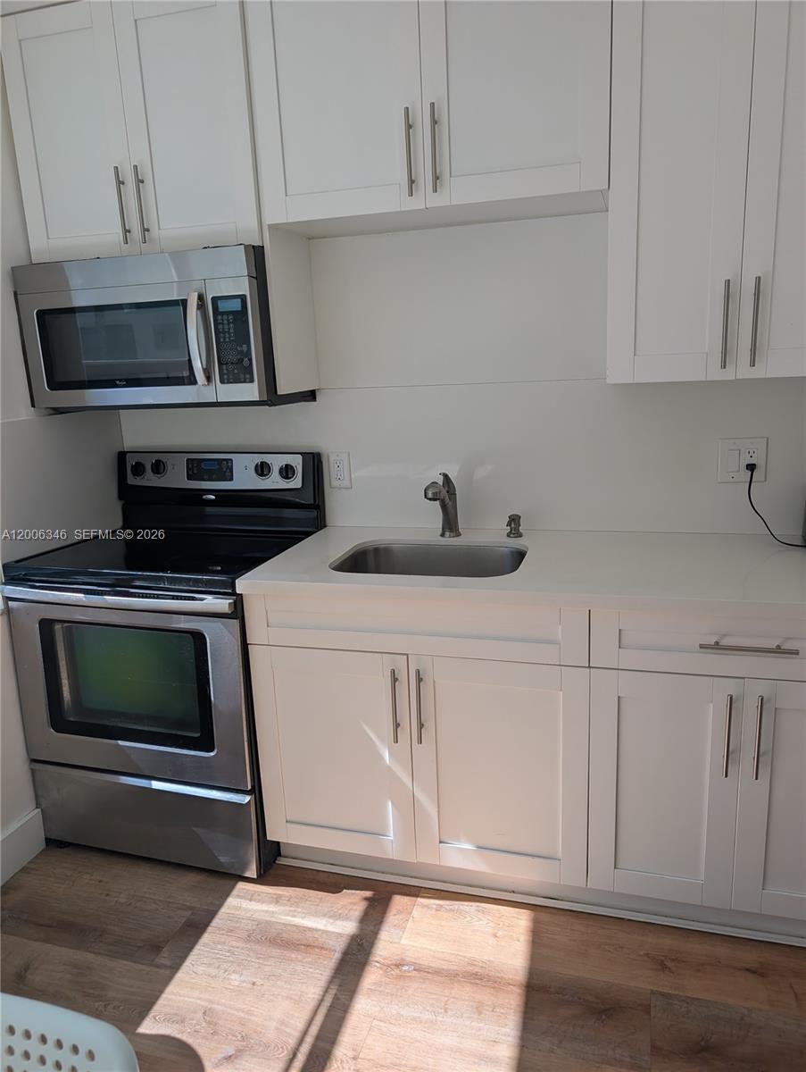A kitchen features white cabinets, stainless steel appliances, a sink, and light wood-look flooring — 326 Wilson St # 201, Hollywood FL 33019, HOLLYWOOD, FL