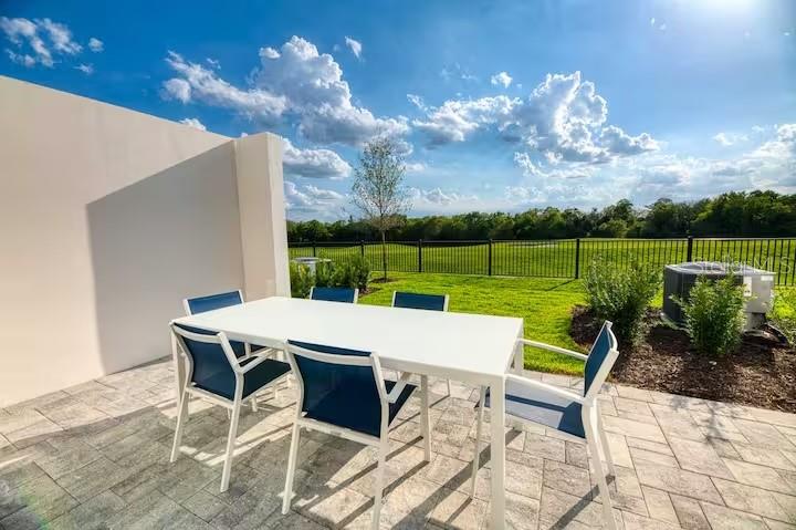 A white patio table and chairs sit on a paved terrace overlooking a grassy field — 792 DRIVING RANGE COURT, REUNION, FL