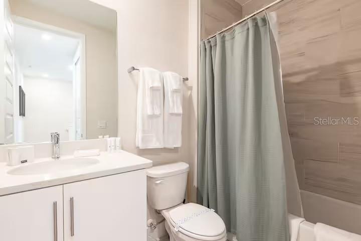 A bathroom features a white vanity, a toilet, and a shower with a sage green curtain — 792 DRIVING RANGE COURT, REUNION, FL