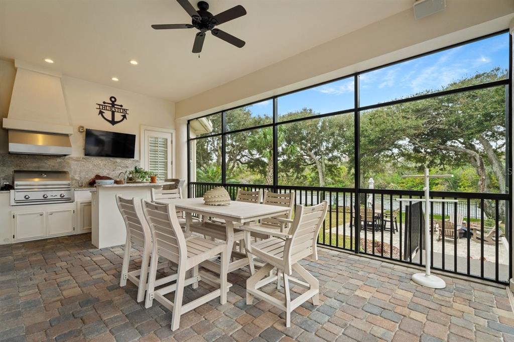 A covered outdoor patio features a dining set, a built-in grill, and screened-in walls — 10 RUE GRANDE MER, PALM COAST, FL