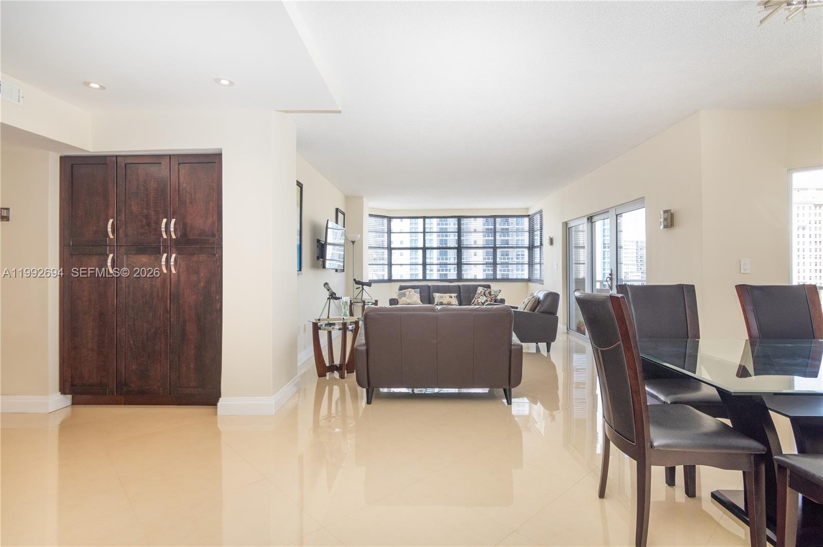 An open-concept living and dining area features tile flooring, dark wood cabinetry, and large windows — 1965 S Ocean Dr # 9F, Hallandale Beach FL 33009, HALLANDALE BEACH, FL